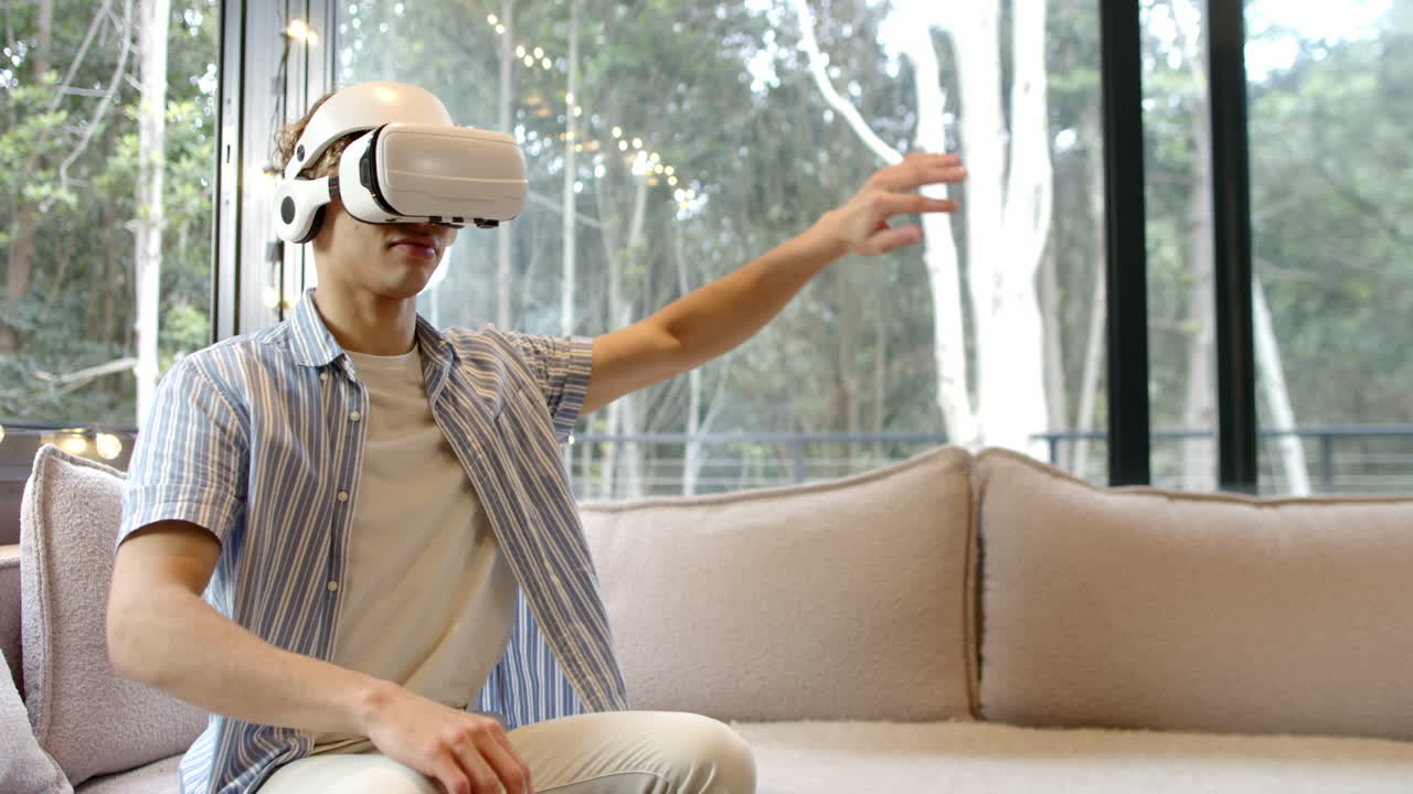 Asian man using VR headset on sofa, enjoying virtual reality experience, copy space