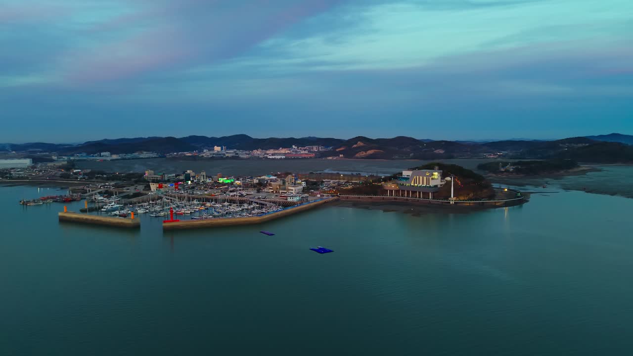 Marina di Jeongok e stazione della funivia di Jebudo durante l'ora blu con faro rosso e lungomare illuminato in Corea del Sud - ripresa aerea con drone in parallasse