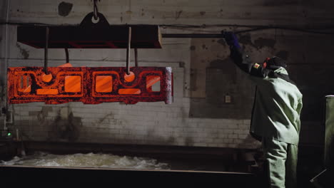 nighttime foundry scene with a focused worker in full safety attire handling the precise movement of searingly hot steel castings, showcasing the intense environment of metal manufacturing