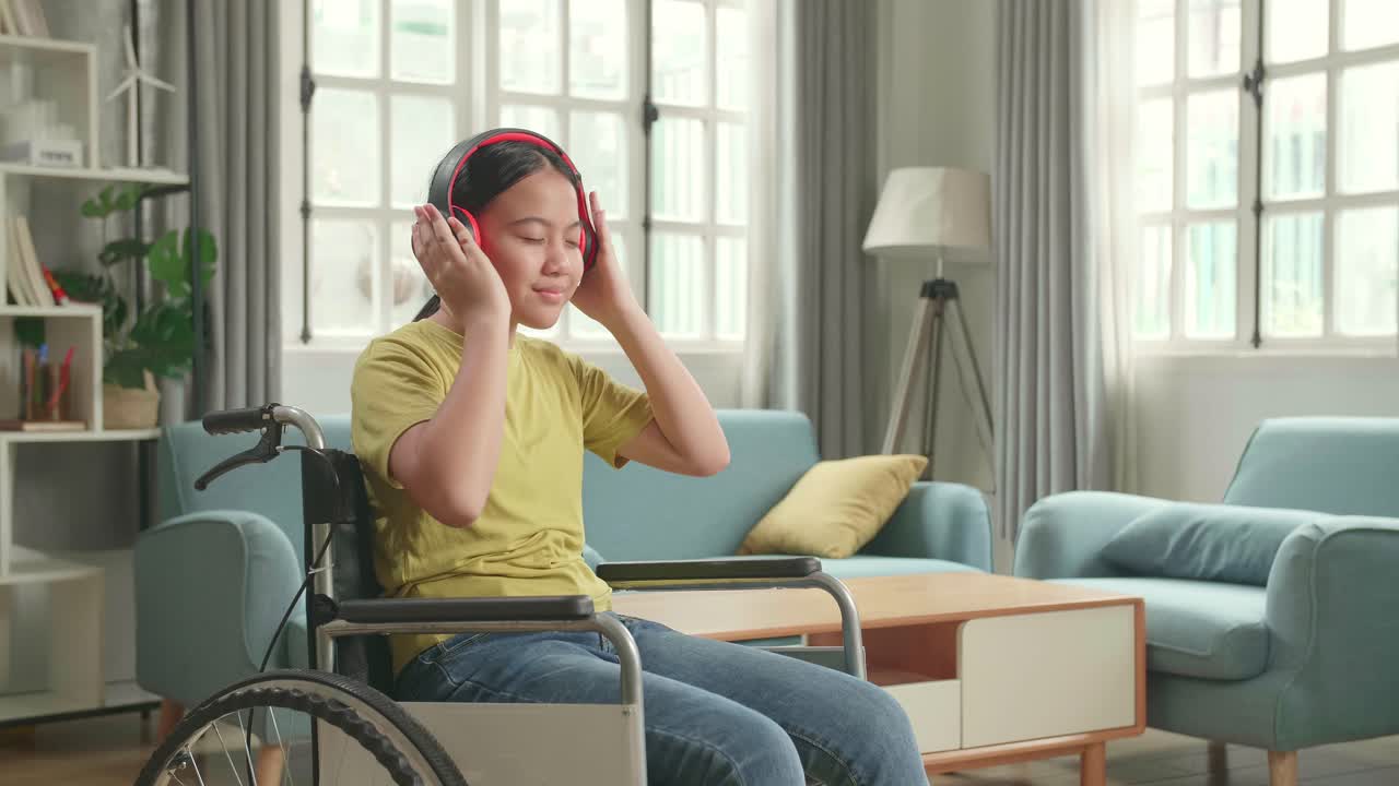 Asian Kid Girl Sitting In A Wheelchair Listening To Music With Headphones And Dancing In Living Room