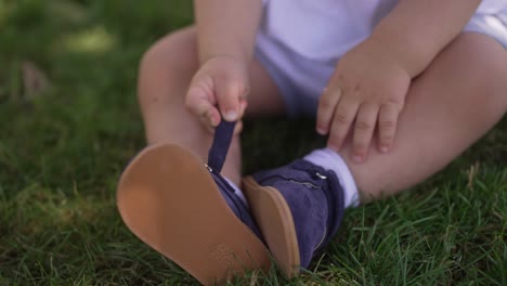 baby sits on grass, fastening a navy shoe strap, focused on their tiny hands