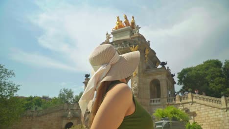 Stunning-footage-of-a-young-caucasian-girl-in-a-green-dress-and-hat-joyfully-posing-in-front-of-Cascada-Monumental---Gaudí's-fountain-in-Parc-de-la-Ciutadella