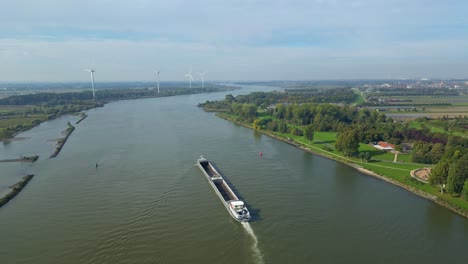 aerial view over barge travelling along oude maas with row of wind turbines seen in distance