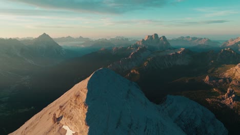 aerial drone view spiraling around the iconic tofana di rozes summit in the italian dolomites at sunrise, with monte pelmo and monte antelao visible in the background