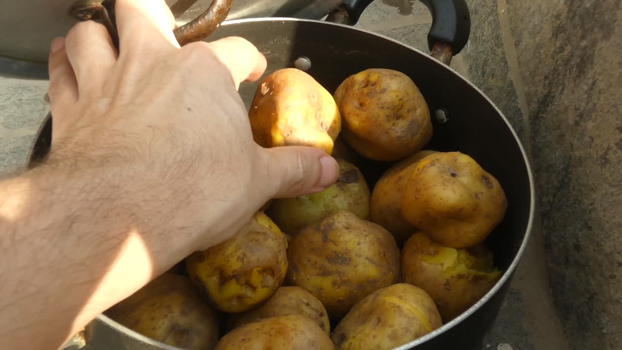 A closed pot lies on the floor. A hand opens the lid revealing it to be full of boiled Peruvian yellow potatoes. The hand picks up a single potatoe and puts it down. Then closes the lid of the pot.