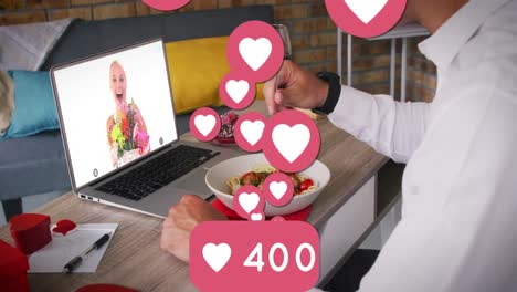 iconos del corazón y números crecientes contra el hombre que almuerza mientras tiene una videollamada en la computadora portátil