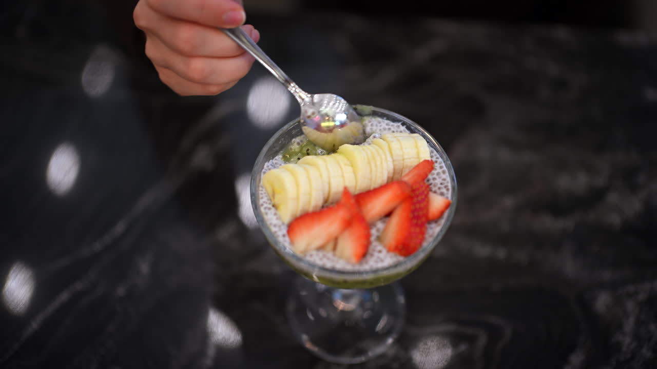Primo piano di un dessert budino di chia servito in un bicchiere, guarnito con fragole a fette e purea di frutta.