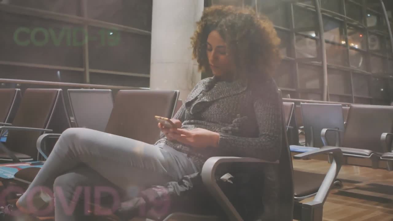 animación de palabras flotantes de covid-19 sobre una mujer de raza mixta que usa un teléfono inteligente en el aeropuerto