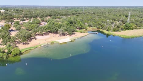 Turning-to-the-left-and-moving-right-showing-shoreline-of-a-public-recreational-area-that-has-a-beach-area,-boats,-and-fishing-dock