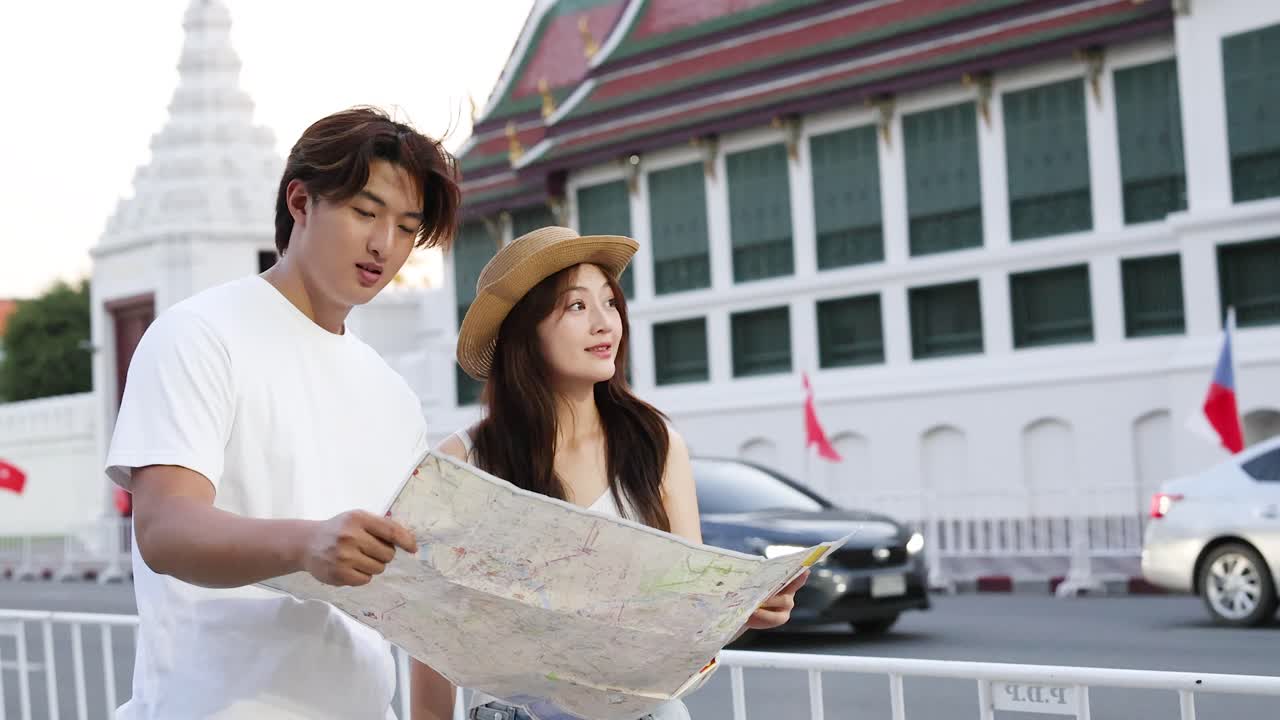 คู่หนุ่มสาวปรึกษาแผนที่กระดาษกลางแจ้ง ฉากถนนในเมือง แสงธรรมชาติ ช่วงเวลาการเดินทางที่เป็นธรรมชาติ