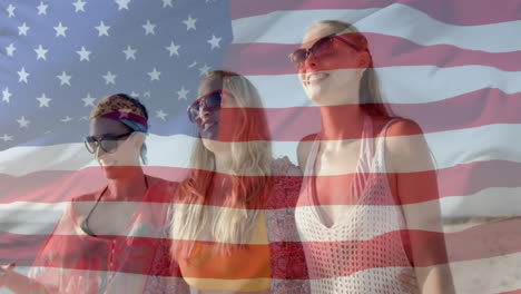 animation of american flag over happy happy caucasian female friends walking on sunny beach