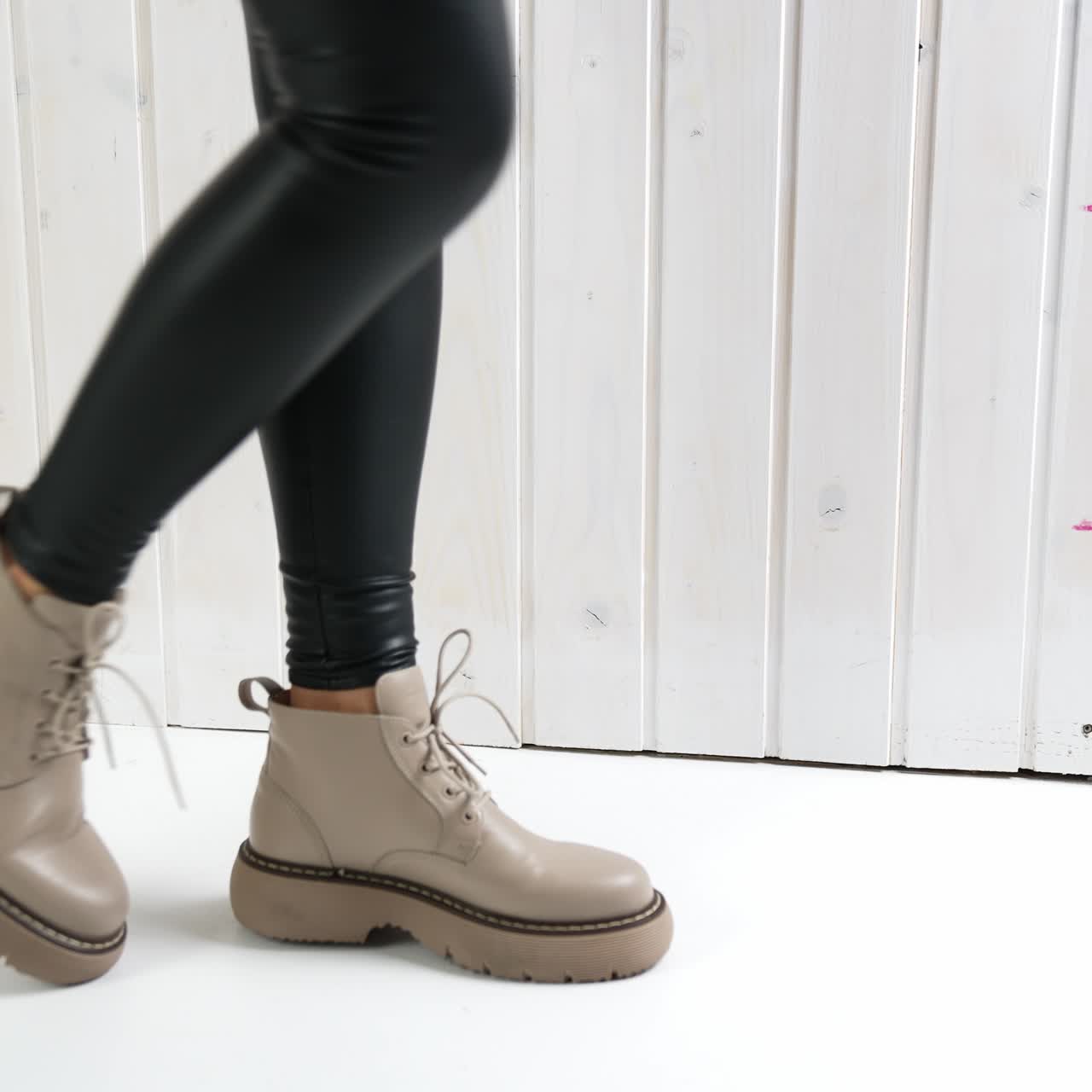 Model posing in beige boots on tractor soles. Woman wearing black leather leggings demonstrating stylish footwear
