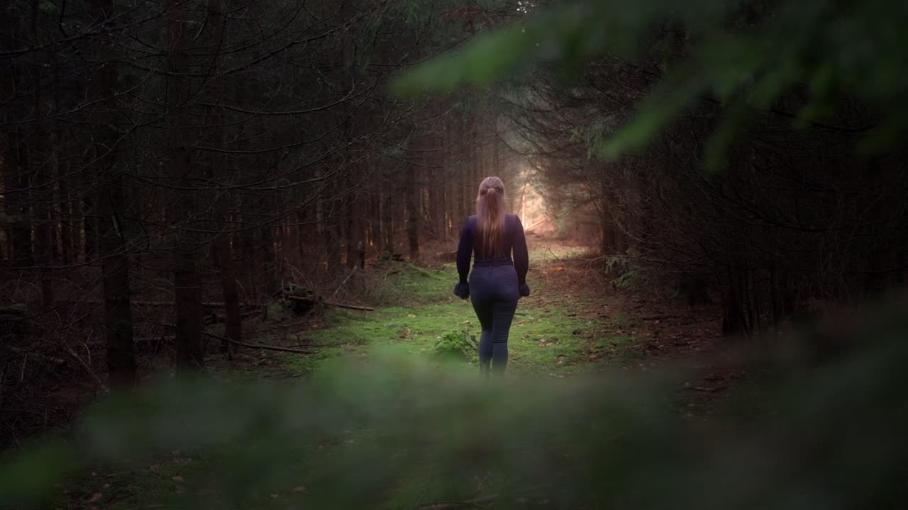 Young girl with long hair walks out into the glow between the trees
