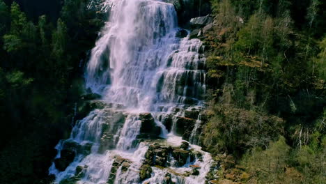 close-up slowmotion drone lifting shot of water falling down from a high waterfall