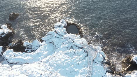 bright sunlight at brimketill rock pool with tourist viewing platform, iceland