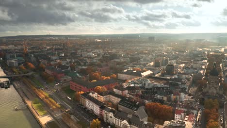 Toma-De-Drones-De-Mainz,-La-Ciudad-De-La-Vacuna-Biontech-Contra-Corona-Covid-19-En-Alemania-Desde-Una-Vista-Aérea-En-Luz-Dorada-De-Otoño-Y-Cielo-Dramático-Sobre-Hojas-De-árboles-Rojizos