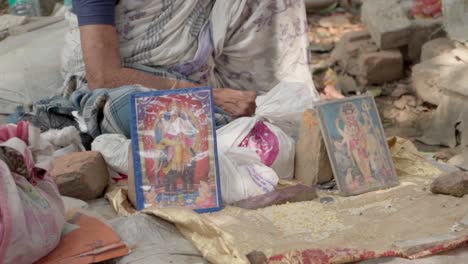 photo frames of indian gods and goddesses beside an unrecognizable old indian woman