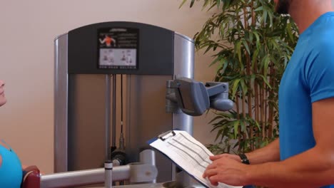 Woman-using-weights-machine-in-gym-with-trainer