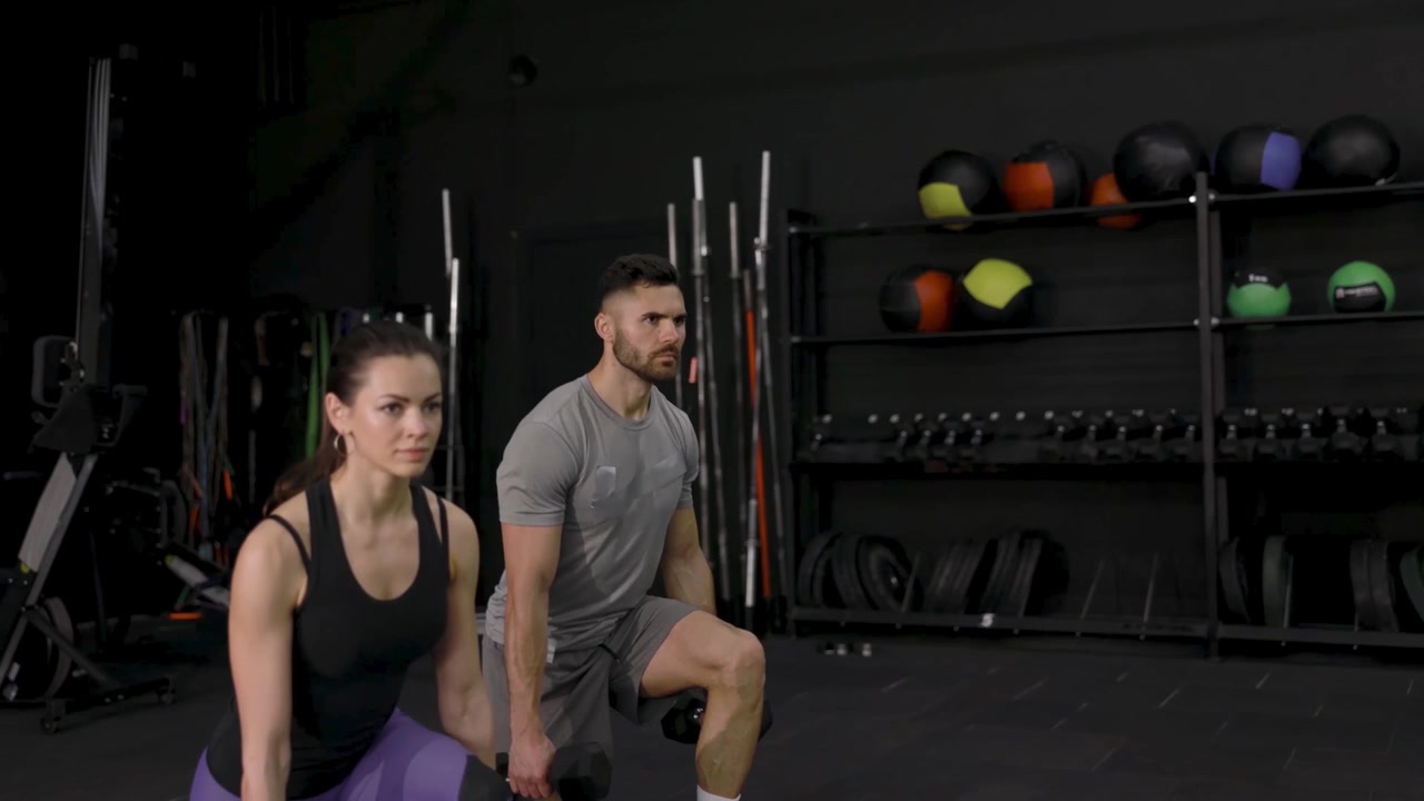 Hombre y Mujer Realizando Zancadas con Mancuernas en un Gimnasio Moderno