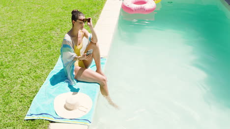 relaxing by pool, woman enjoying sunny day with smartphone and sunhat nearby, copy space
