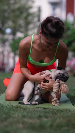 woman practicing yoga with her pug dog in the park