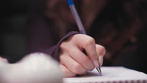 close up of female hand holding pen while writing on notebook page. fingernails with light polish visible, background blurred to emphasize delicate movement and attention to detail in calm atmosphere