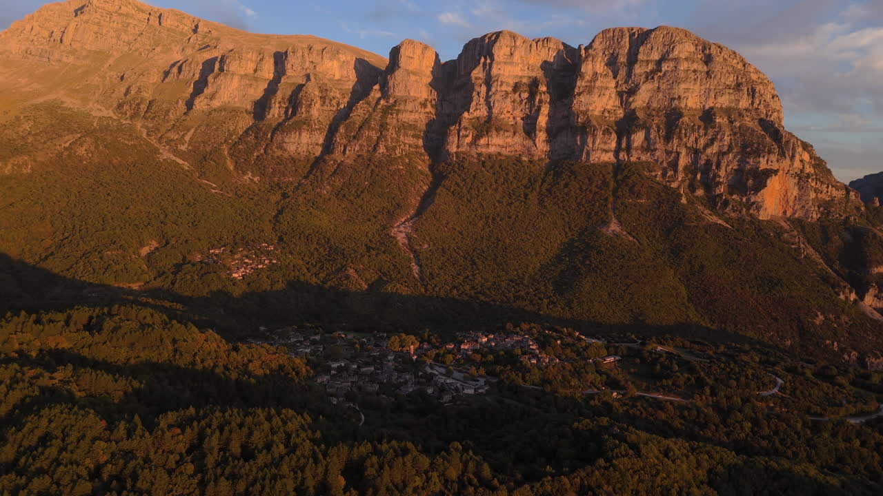 Aerial overview descends to Papigo village at sunset, nestled in Zagori mountains with warm light and shadows