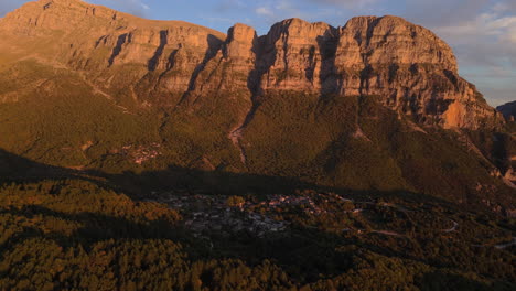 aerial overview descends to papigo village at sunset, nestled in zagori mountains with warm light and shadows