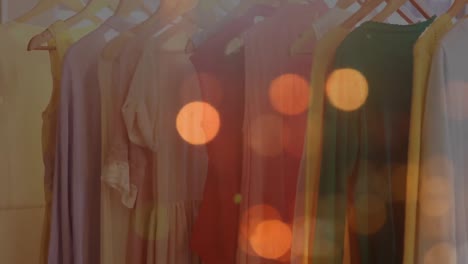 Animation-of-bokeh-lights-over-clothes-hanging-on-display-in-shop