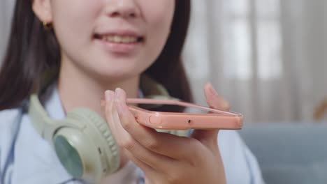 close up of asian teen girl's hands holding smartphone to record voice while sitting on sofa in the living room at home