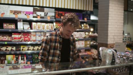 portrait of handsome man in plaid shirt walking and looking around in supermarket. mature guy in 30s searching for products while doing shopping in grocery store. staring at showcase