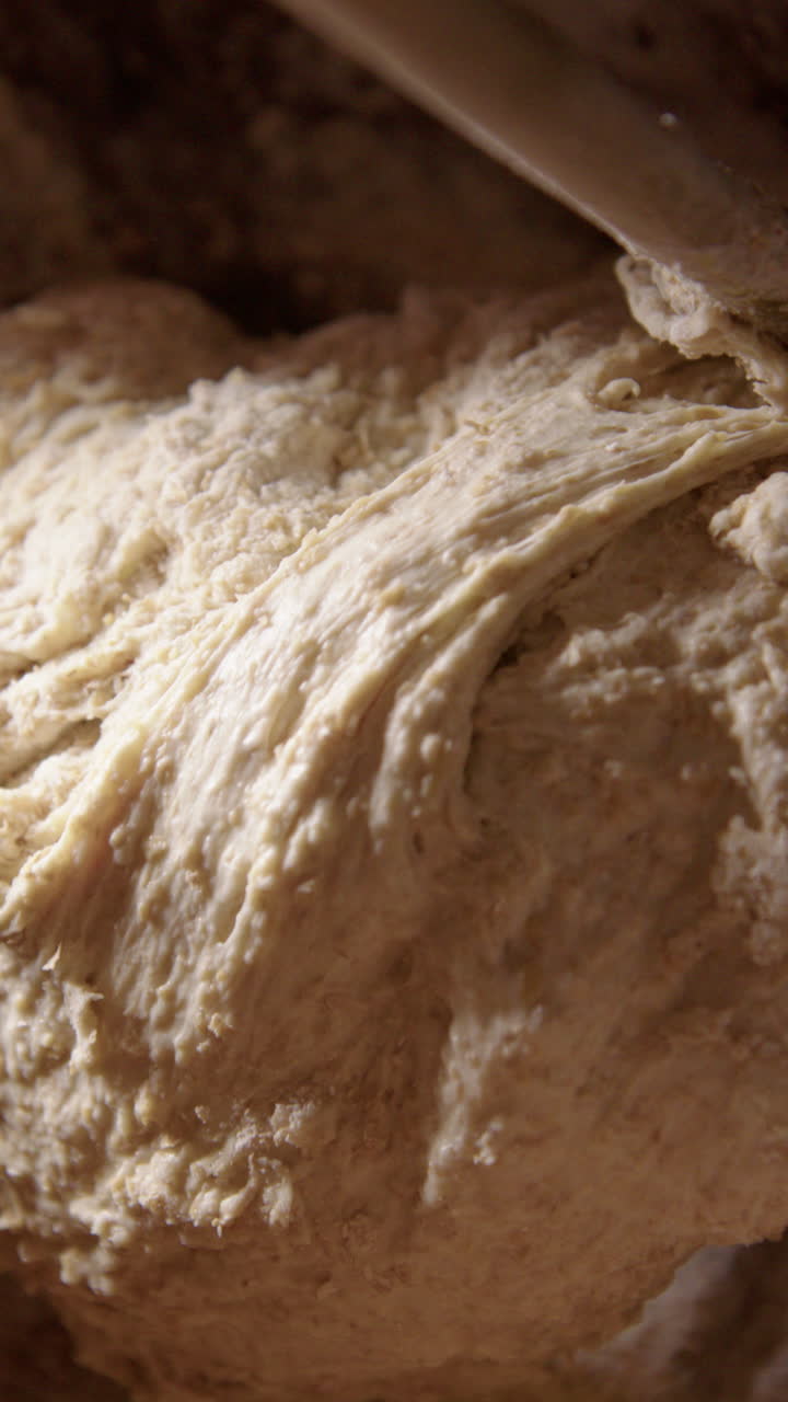 Organic sourdough bread dough is helped into clay baker with wooden spoon