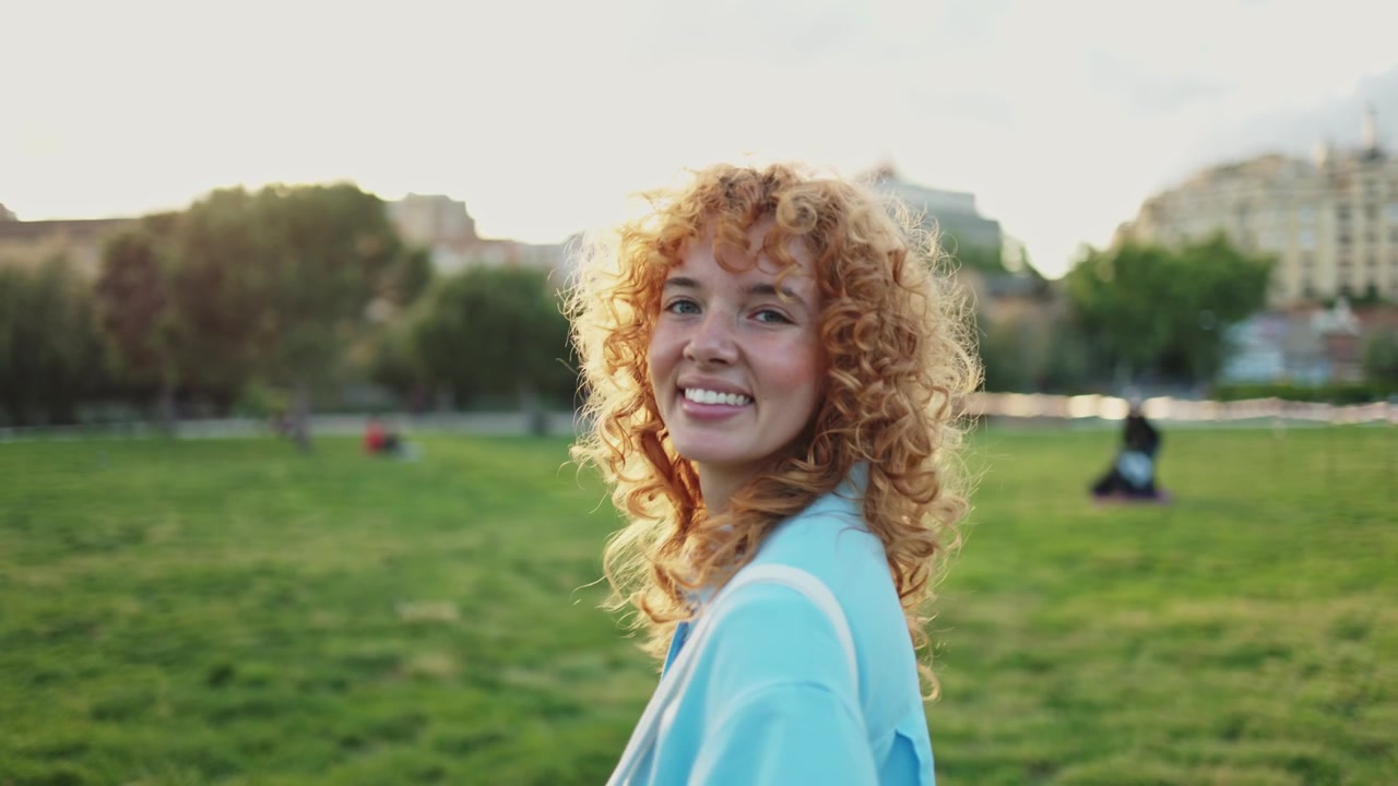 Happy Young Woman with Curly Red Hair Smiling in a Sunny Park