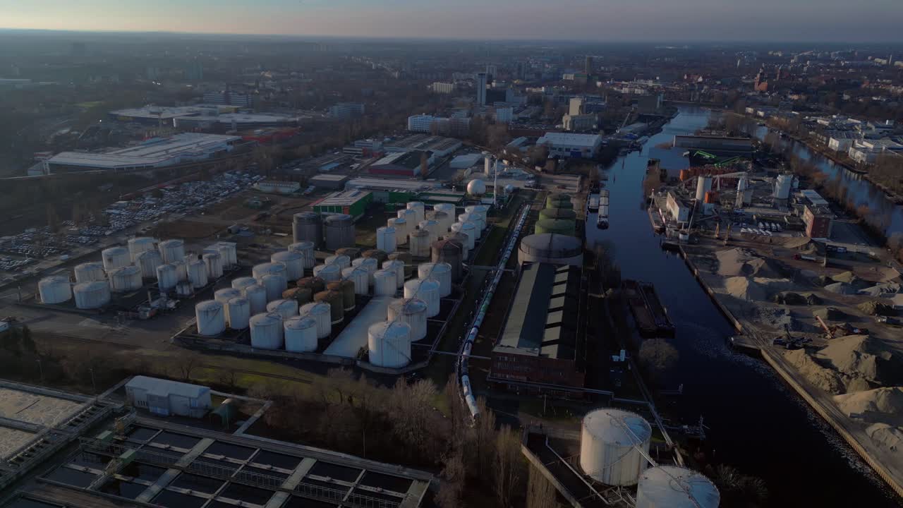 Berlin biogas plant with its large white tanks reflecting on the river next to it during sunset. Fabulous aerial view flight static tripod hovering drone