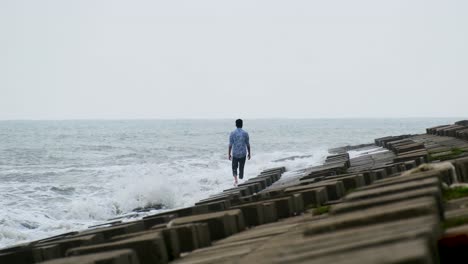 man is walking alone over block concrete sea walls with rough waves