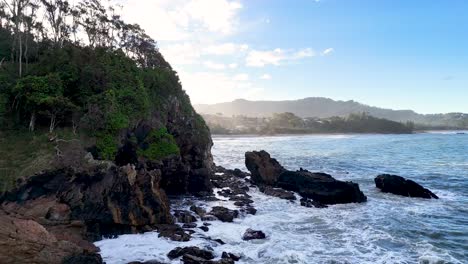 waves crash against rocky cliffs under clear skies at charlesworth bay beach, coffs harbour, australia. lush greenery and serene ocean views