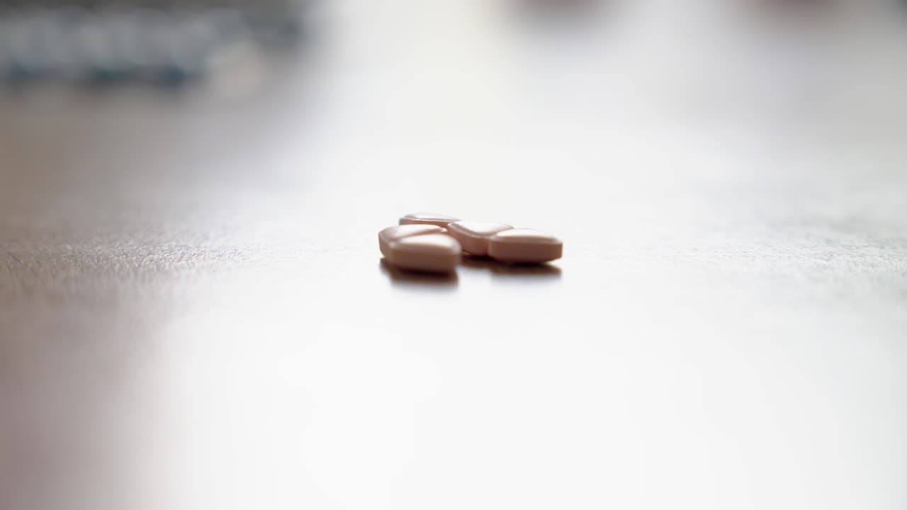 Fingers reach to collect medication pills on a smooth wooden table