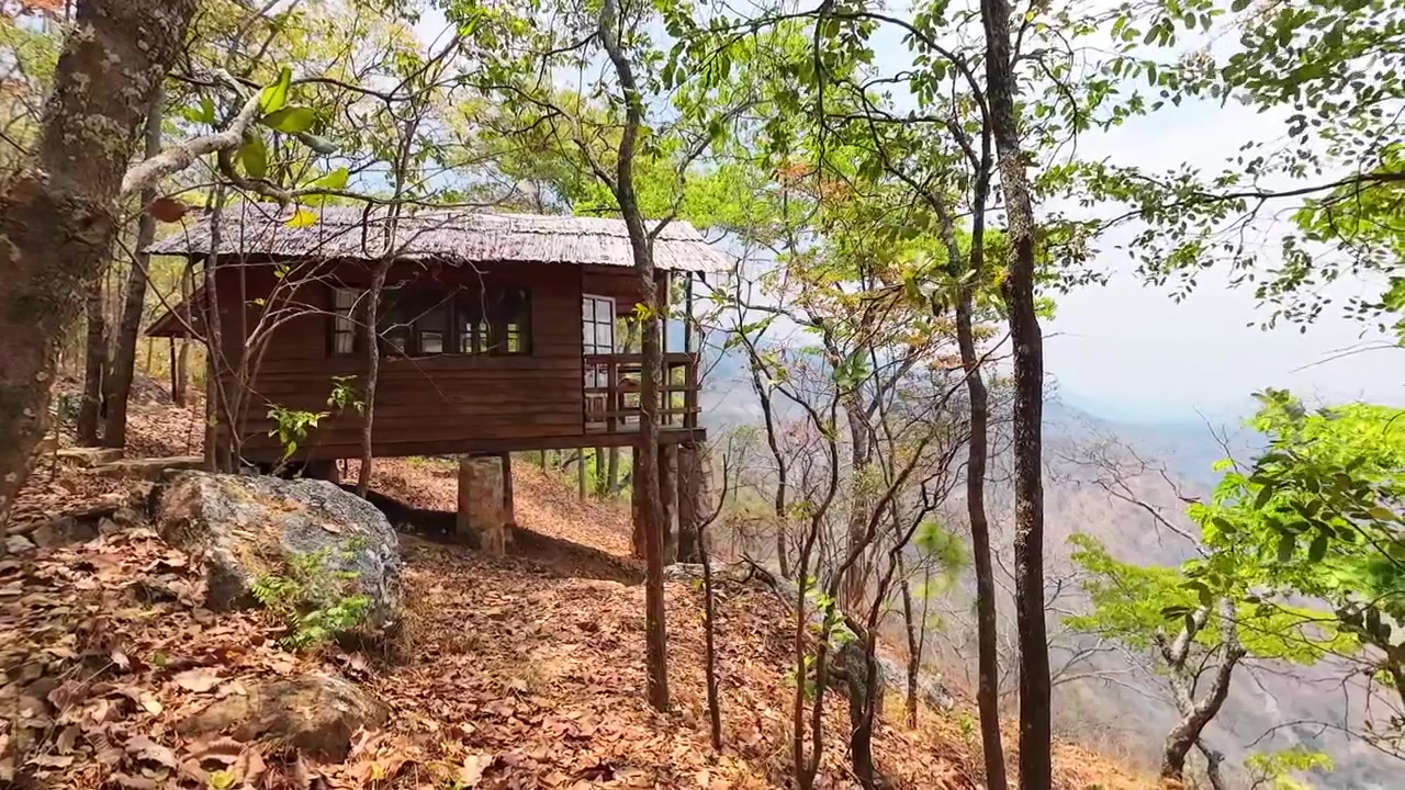 Cabina sulla scogliera con finestre e un balcone si affaccia su una drammatica scarpata boscosa vicino a Livingstonia, Malawi, mentre gli alberi circostanti ondeggiano al vento.
