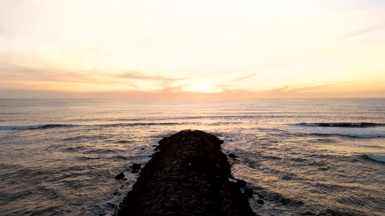 Onde si infrangono dolcemente su un sentiero roccioso che si estende nel mare al tramonto.