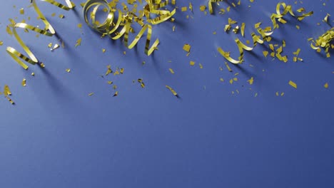 Video-of-gold-streamers-and-confetti-on-dark-blue-background,-with-copy-space