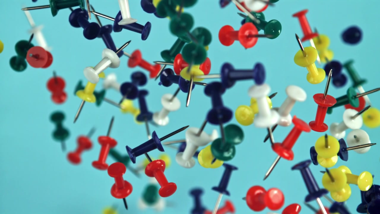 Slow motion di puntine colorate che cadono su uno sfondo blu.