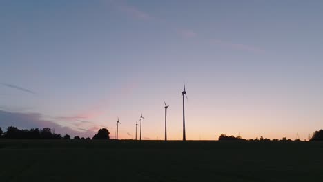 Vista-Aérea-De-Establecimiento-De-Turbinas-Eólicas-Que-Generan-Energía-Renovable-En-Un-Parque-Eólico,-Por-La-Noche-Después-De-La-Hora-Dorada-Del-Atardecer,-Paisaje-Rural,-Siluetas-De-Alto-Contraste,-Disparo-De-Drones-Retrocediendo