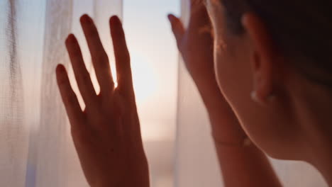 close-up-young-woman-gently-opening-curtains-looking-out-window-at-beautiful-sunrise