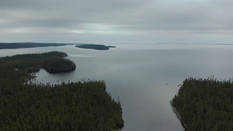 aerial shot over a huge lake and forest on a cloudy day showing a small isolated cabin
