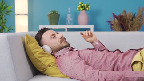 man relaxing on sofa at home with headphones listening to music, daydreaming and happy.