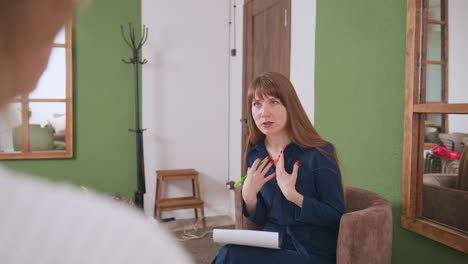 therapist seated in calming space talks with client while using expressive hand gestures to communicate empathetically during therapeutic session, promoting emotional clarity in supportive atmosphere