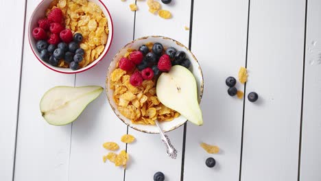 copos de maíz dorados con frutas frescas de frambuesas, arándanos y pera en tazón de cerámica