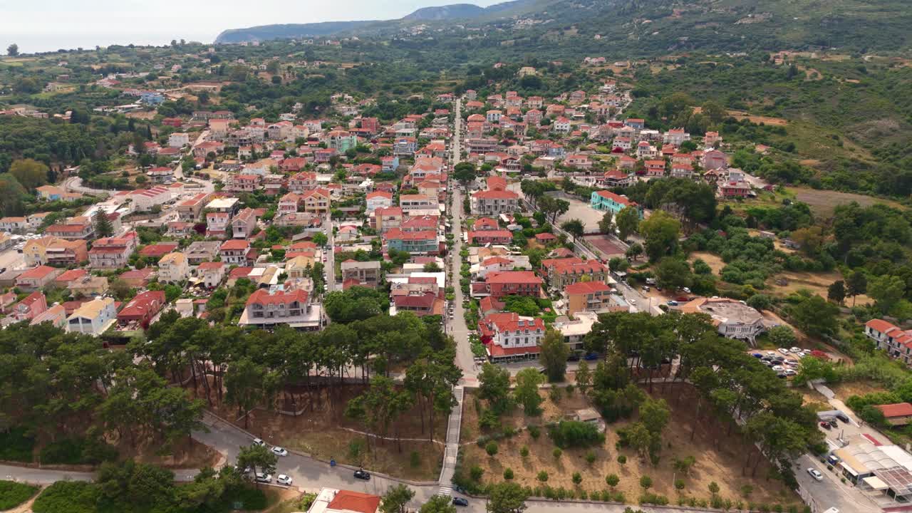 Serene aerial view of Skala, Kefalonia at sunset, highlighting iconic Greek structures, bustling town life, and vivid landscapes under a glowing Mediterranean sky.