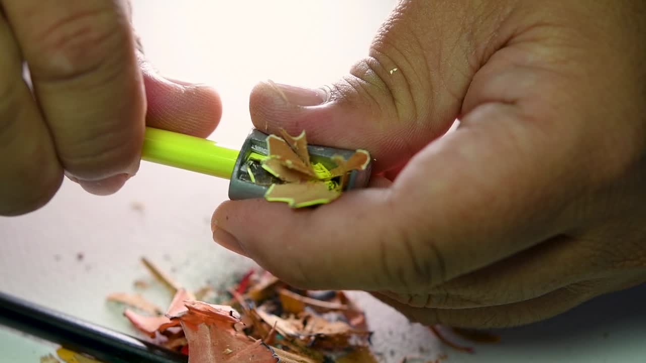 쐐기형 연필깎이로 연필과 색연필을 천천히 깎는 손의 영상