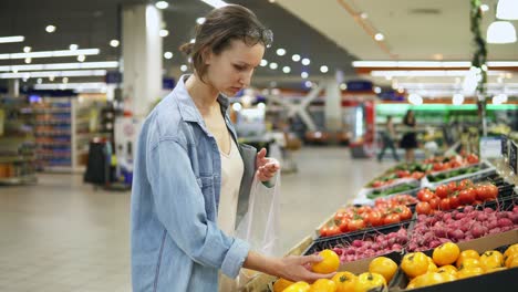 Shopping.-Woman-choosing-bio-food-yellow-tomato-in-vegetable-store-or-supermarket.-Takes-one-by-one-and-puts-it-in-a-cellophane-bag.-Yellow-fresh-tomatos